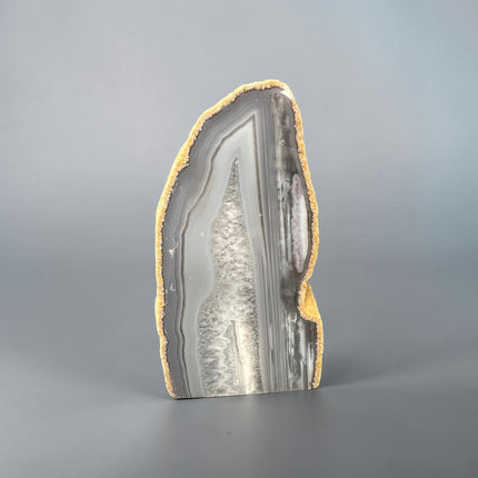 Grey and white agate cut base with natural quartz inclusions weighing 522 grams standing upright on a polished flat base from Raven's Cauldron.
