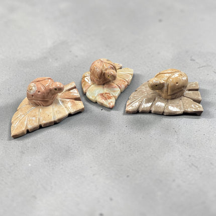 Hand-carved soapstone ladybug resting on a leaf measuring 3 x 2.25 x 1 inches, symbolic of good luck, prosperity, and nature, available from Raven's Cauldron.