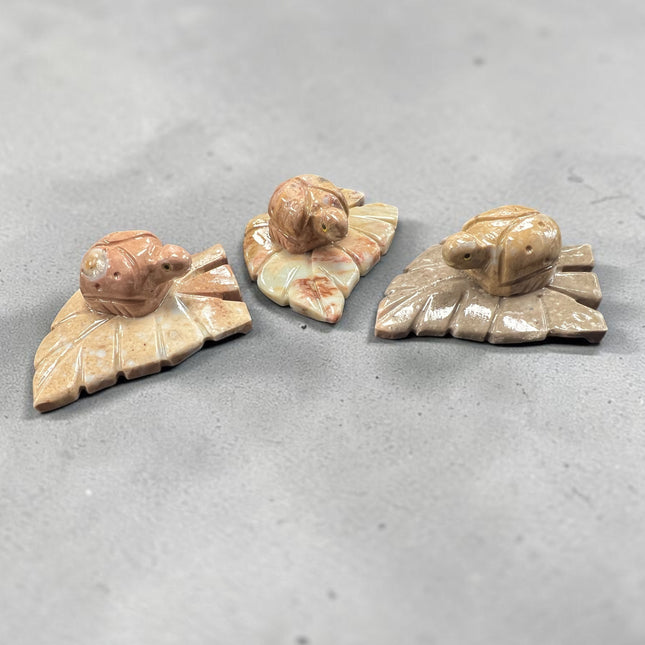 Hand-carved soapstone ladybug resting on a leaf measuring 3 x 2.25 x 1 inches, symbolic of good luck, prosperity, and nature, available from Raven's Cauldron.