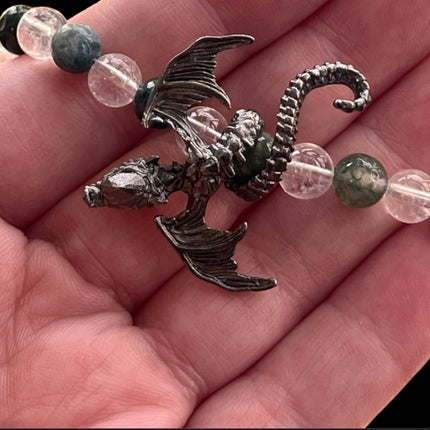 Silver dragon charm on a necklace with clear and green beads held in hand