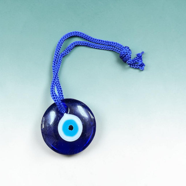 Blue glass Evil Eye charm pendant on a blue cord necklace featuring a traditional protective symbol measuring approximately 1 inch.