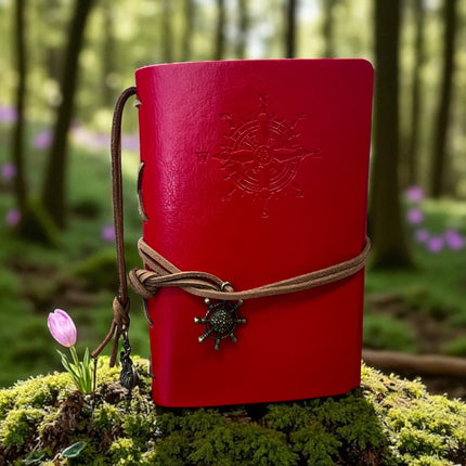 Red notebook with a compass design on a mossy rock in a forest setting Raven's Cauldron,  6 N. Sandusky St, Delaware, OH 43015
