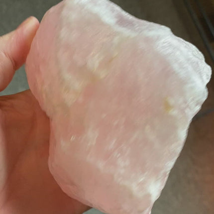 Extra large rose quartz rough displayed, showcasing its natural raw beauty with pink hues and crystalline texture.  Close-up image of an extra large rough rose quartz chunk highlighting its unpolished and jagged form.Massive raw rose quartz piece, exhibiting its pure and untouched state with a soft pink color palette.